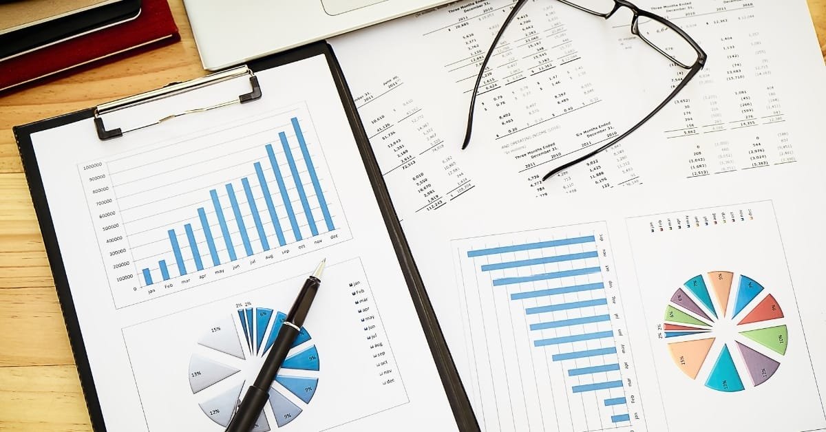 A close-up of a business earnings statement being edited by a professional with a pen and eyeglasses on the desk